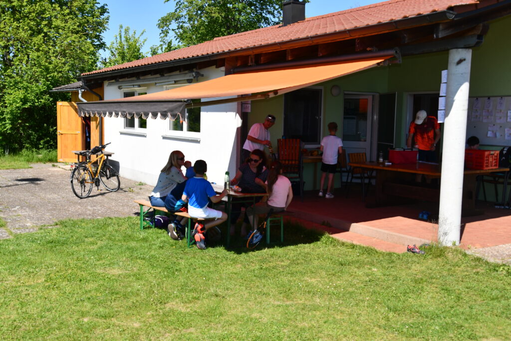 Blick auf das Tennisheim des FC Horgau und Spieler, die gemütlich zusammen sitzen.